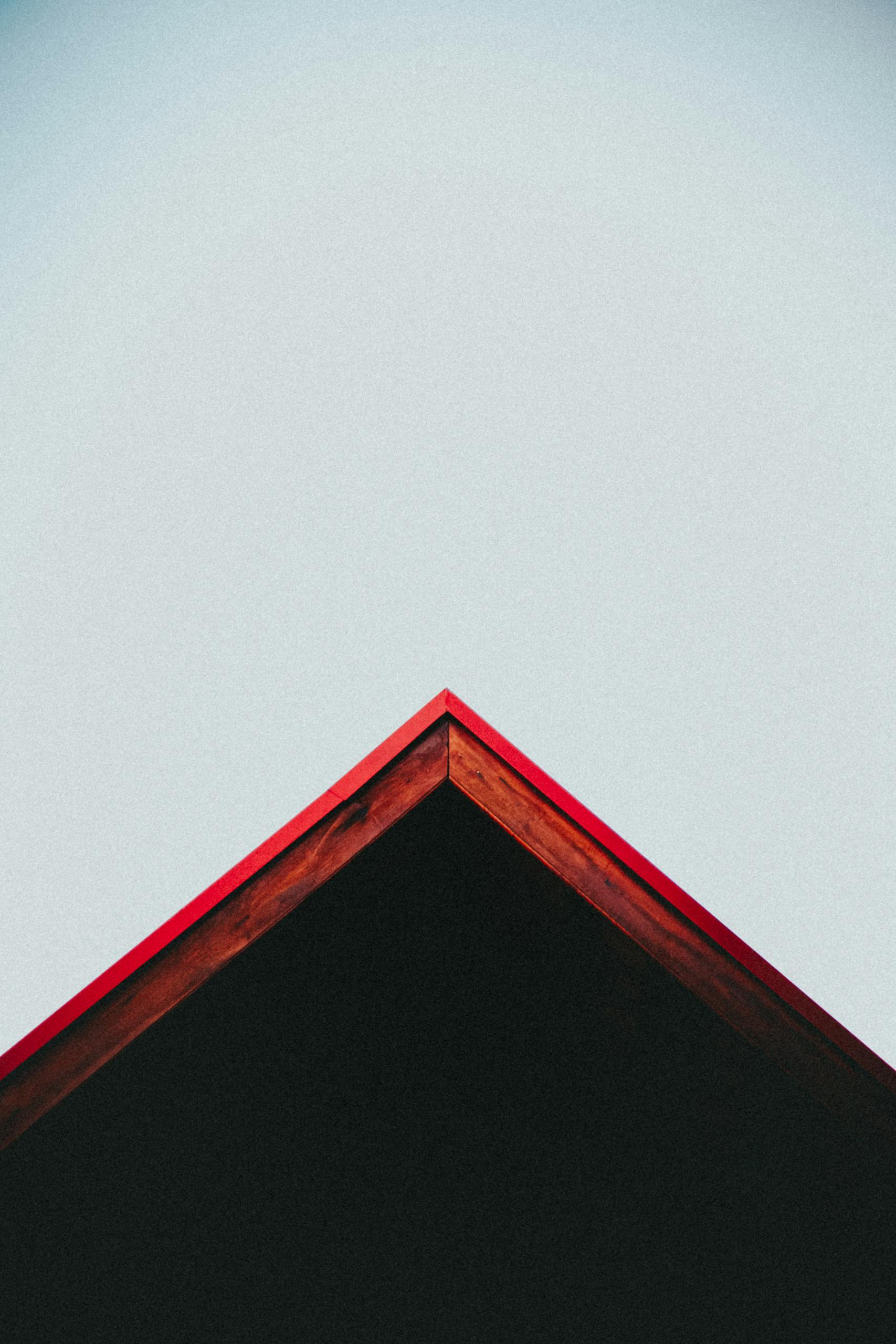 Artistic view of a red roof peak contrasting with a clear blue sky.